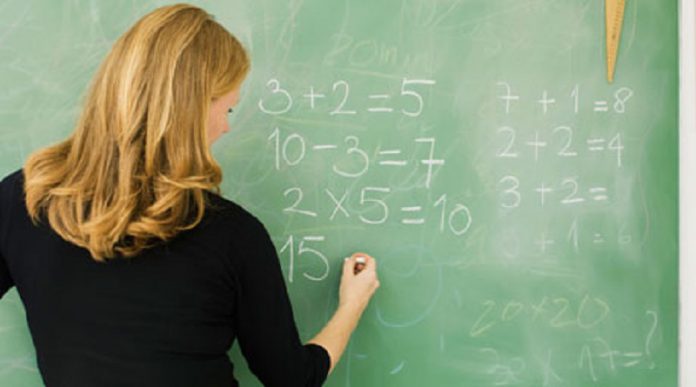 Elementary teacher writing arithmetic on blackboard, rear view